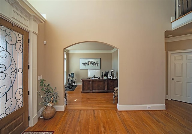 entrance foyer with light wood-style flooring, a high ceiling, arched walkways, and crown molding