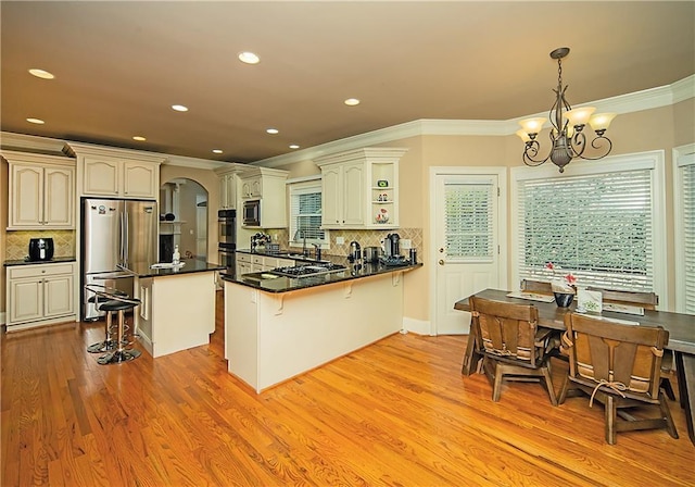 kitchen featuring arched walkways, dark countertops, light wood-style flooring, a kitchen breakfast bar, and stainless steel appliances