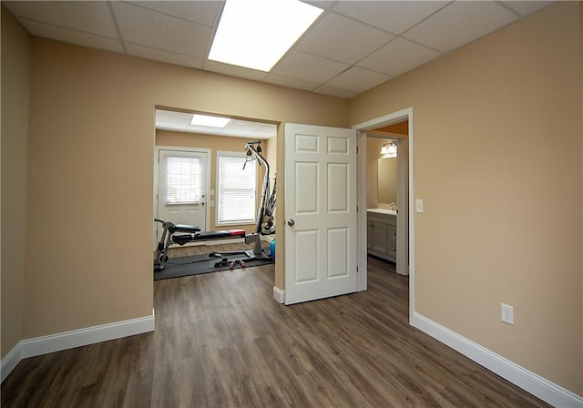 spare room with baseboards, a drop ceiling, and dark wood-style flooring