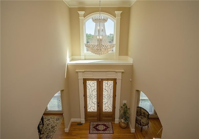 foyer with a wealth of natural light, a notable chandelier, baseboards, and wood finished floors