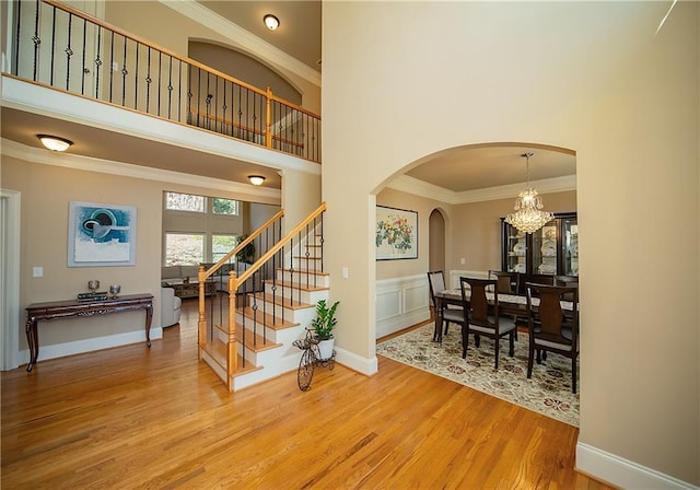 entryway with a notable chandelier, a high ceiling, wood finished floors, stairway, and crown molding