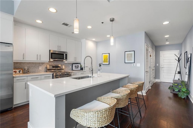 kitchen with pendant lighting, dark hardwood / wood-style flooring, an island with sink, and stainless steel appliances