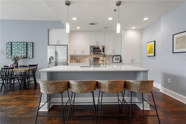 kitchen featuring dark wood-type flooring, white cabinets, stainless steel appliances, and a center island with sink