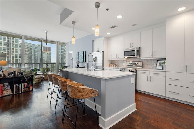 kitchen with pendant lighting, an island with sink, stainless steel appliances, and dark hardwood / wood-style floors