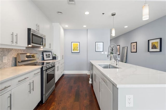 kitchen featuring stainless steel appliances, tasteful backsplash, dark wood-type flooring, a kitchen island with sink, and a sink