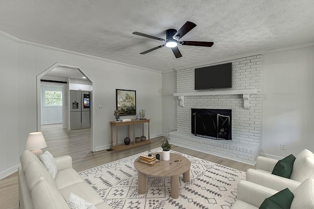 living room featuring a brick fireplace, ceiling fan, a textured ceiling, and light wood-type flooring