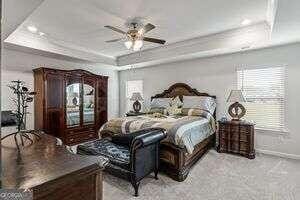 carpeted bedroom featuring a tray ceiling and ceiling fan