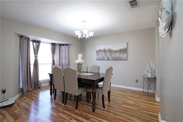 dining space featuring a notable chandelier, light hardwood / wood-style flooring, and a textured ceiling