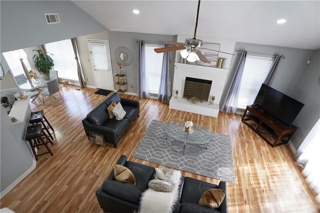 living room featuring lofted ceiling, light wood-type flooring, a wealth of natural light, and a fireplace