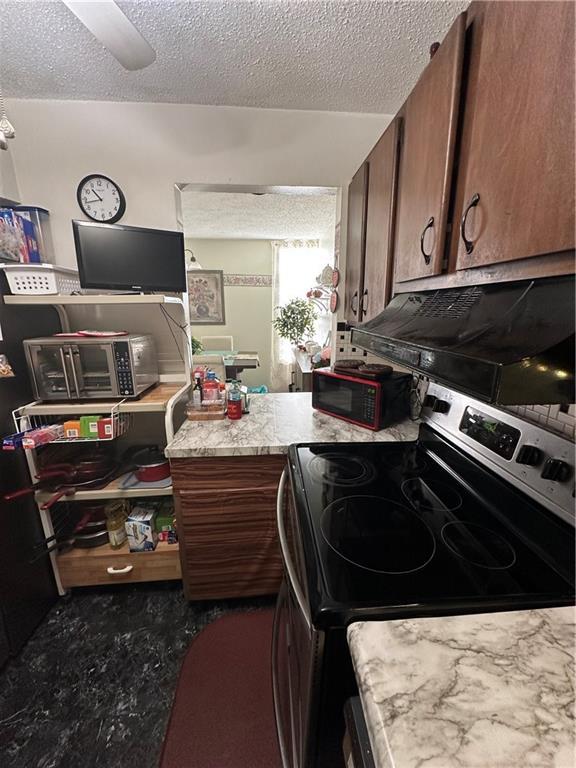 kitchen featuring ceiling fan, stainless steel electric stove, range hood, and a textured ceiling