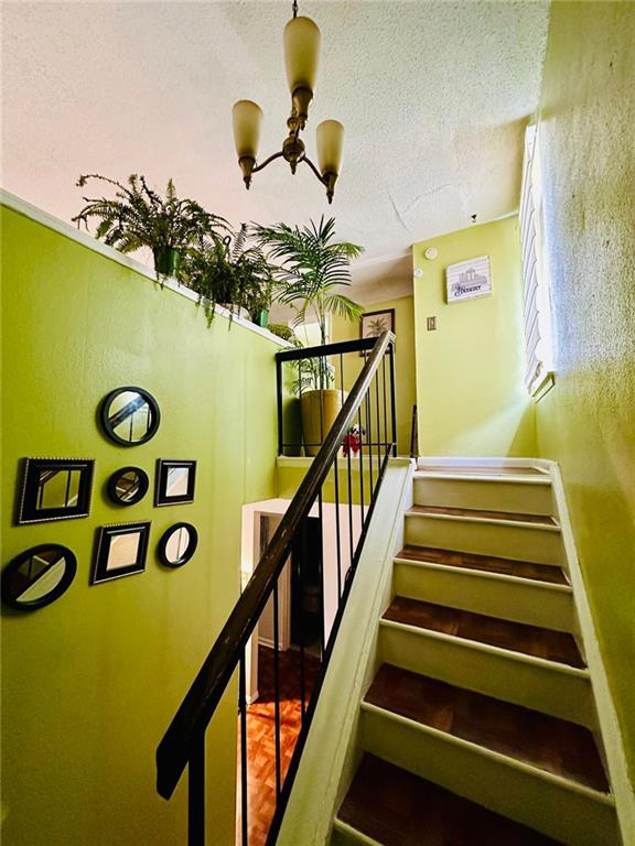 staircase with a notable chandelier, parquet flooring, and a textured ceiling