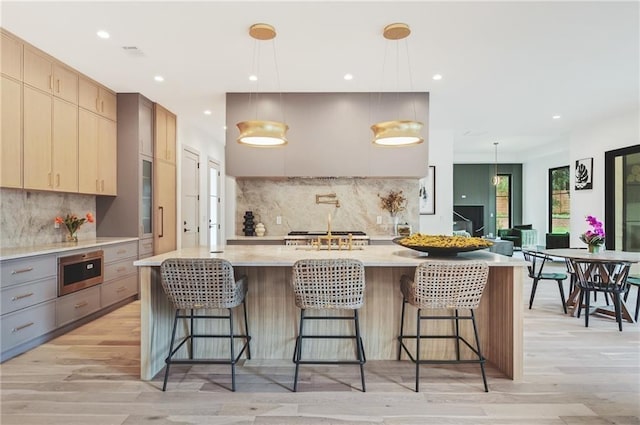 kitchen with light stone counters, decorative light fixtures, a kitchen island, and light brown cabinets