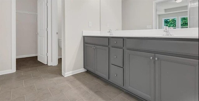 full bathroom with a sink, toilet, baseboards, and double vanity