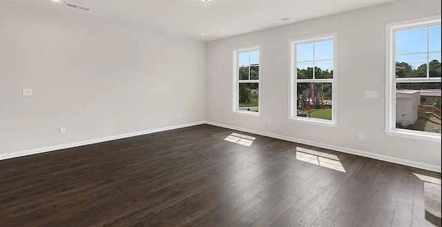 empty room with visible vents, a healthy amount of sunlight, dark wood-type flooring, and baseboards