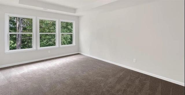 unfurnished room featuring a tray ceiling, baseboards, and dark carpet