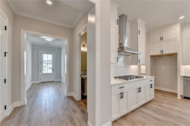 kitchen featuring tasteful backsplash, stainless steel appliances, light wood finished floors, wall chimney exhaust hood, and white cabinetry