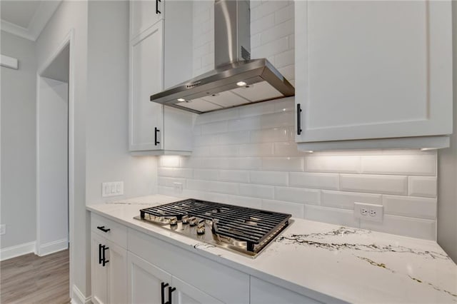 kitchen featuring stainless steel gas stovetop, white cabinets, wall chimney exhaust hood, baseboards, and decorative backsplash