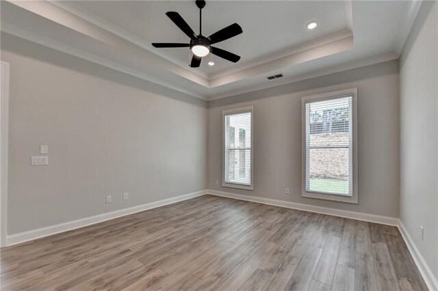 spare room featuring a tray ceiling, ornamental molding, light wood-style floors, baseboards, and ceiling fan