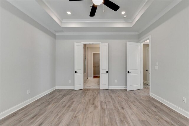 unfurnished bedroom with baseboards, a tray ceiling, light wood-style floors, and crown molding