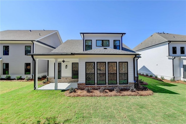 back of property with brick siding, a patio area, a lawn, a shingled roof, and ceiling fan