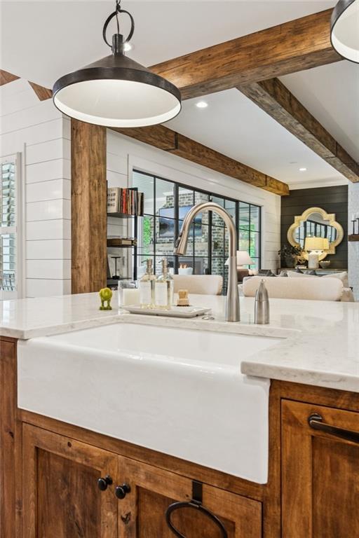 150 Trinity Farm Dr, Canton, GA 30115 - kitchen featuring beamed ceiling, brown cabinetry, open floor plan, light stone counters, and wood walls