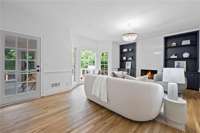1017 Mill Creek Mnr NE, Brookhaven, GA 30319 - living area with a warm lit fireplace, light wood finished floors, built in features, a chandelier, and crown molding