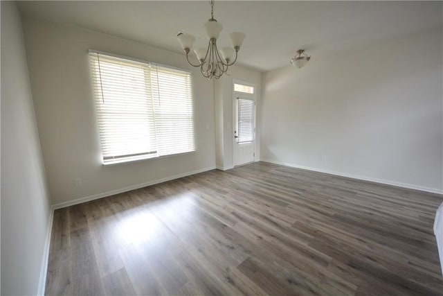 spare room featuring a notable chandelier, wood finished floors, and baseboards