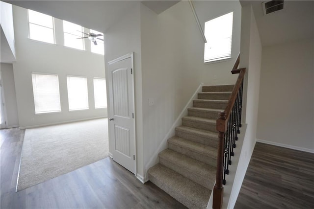 stairs with visible vents, a ceiling fan, wood finished floors, a high ceiling, and baseboards