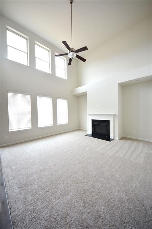 unfurnished living room with a fireplace with flush hearth, a ceiling fan, carpet floors, a high ceiling, and baseboards