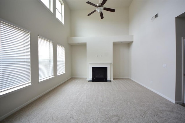 unfurnished living room with visible vents, a fireplace with flush hearth, carpet floors, baseboards, and ceiling fan