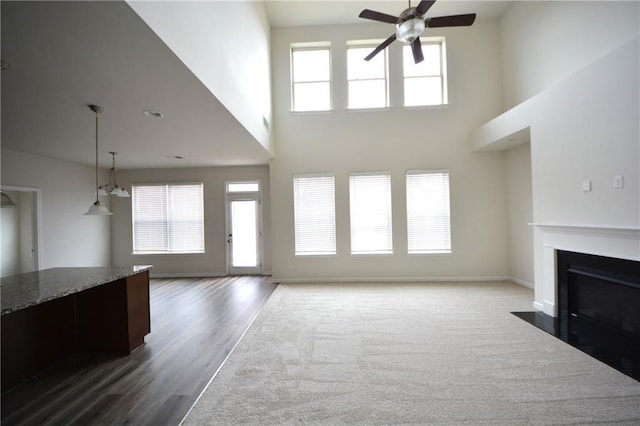 unfurnished living room with a fireplace with flush hearth, wood finished floors, baseboards, and ceiling fan