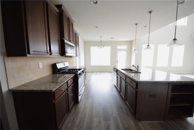 kitchen featuring tasteful backsplash, dark brown cabinetry, dark stone countertops, stainless steel appliances, and a sink