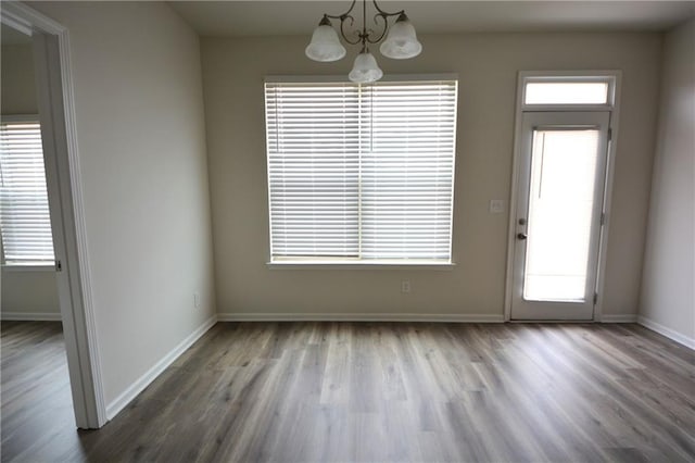 unfurnished dining area with baseboards, an inviting chandelier, and wood finished floors