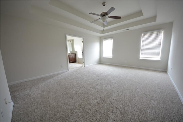 unfurnished bedroom with light carpet, visible vents, baseboards, and a tray ceiling