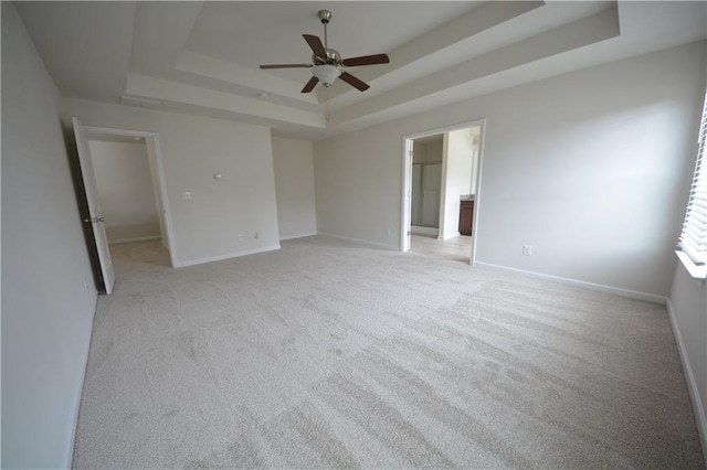 unfurnished bedroom with ceiling fan, a raised ceiling, baseboards, and light carpet