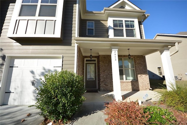 view of exterior entry with an attached garage, covered porch, and brick siding