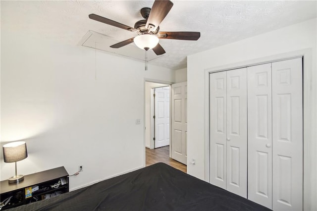 unfurnished bedroom with ceiling fan, a textured ceiling, a closet, and hardwood / wood-style floors