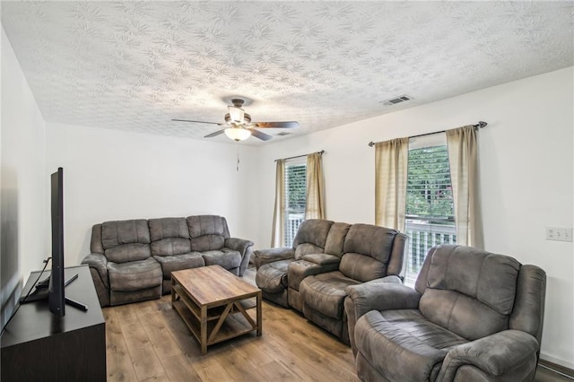 living room with light wood-type flooring, ceiling fan, and a textured ceiling