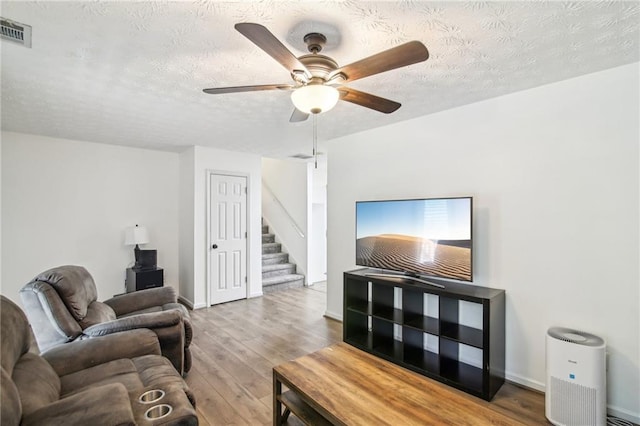 living room featuring wood-type flooring, a textured ceiling, and ceiling fan