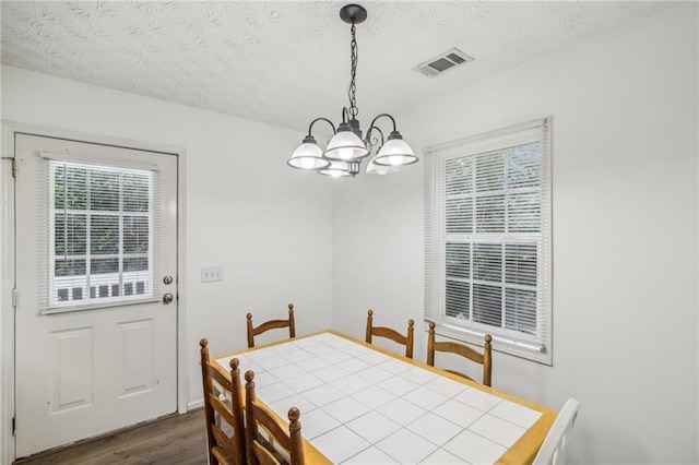 dining space with dark wood-type flooring, a notable chandelier, and a textured ceiling