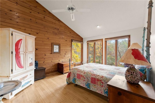 bedroom featuring vaulted ceiling, ceiling fan, light wood-type flooring, and wood walls