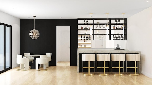 bar featuring sink, decorative light fixtures, and light hardwood / wood-style flooring