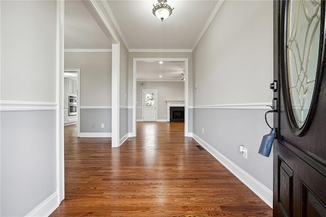 foyer with a fireplace, baseboards, crown molding, and wood finished floors