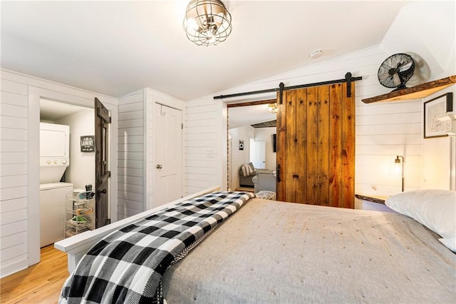 527 Main St, Suwanee, GA 30024 - bedroom featuring stacked washer / drying machine, lofted ceiling, a barn door, light wood-style floors, and wood walls