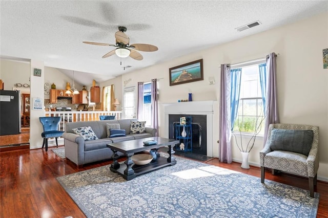 living room with vaulted ceiling, dark wood-type flooring, ceiling fan, and a textured ceiling