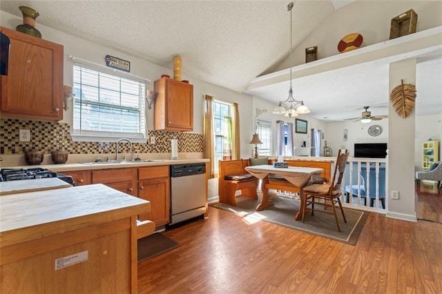 kitchen with sink, decorative light fixtures, vaulted ceiling, dishwasher, and light hardwood / wood-style floors