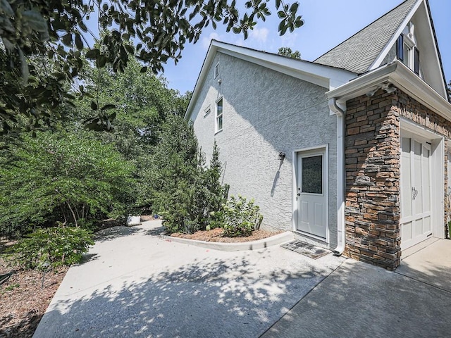 view of side of property with a garage, stone siding, and stucco siding