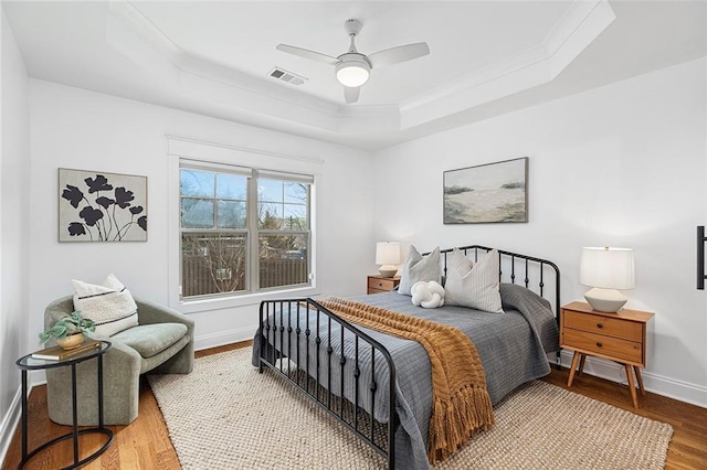 bedroom with visible vents, a tray ceiling, wood finished floors, baseboards, and ceiling fan