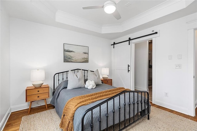 bedroom with a barn door, wood finished floors, baseboards, and a tray ceiling