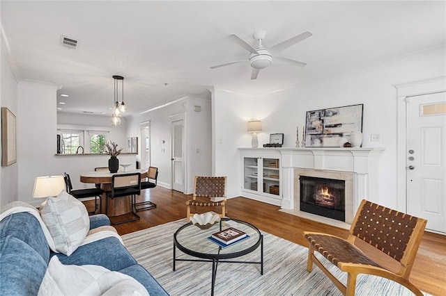 living room with crown molding, wood finished floors, visible vents, and ceiling fan